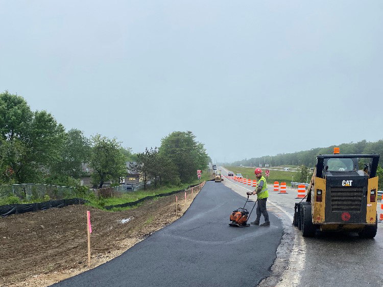 Workers smooth poured asphalt for new temporary off ramp.